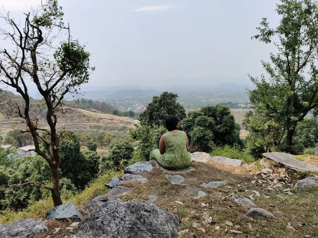 A person sitting quietly on a hilltop, looking out over a wide valley